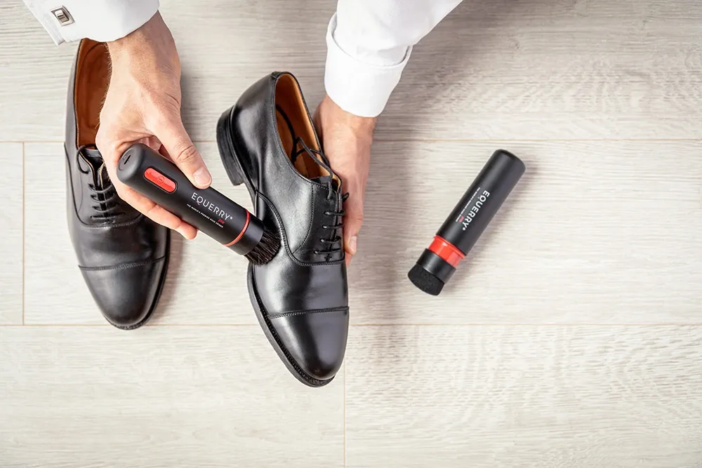A man's hands uses an Equerry Pro shoe shiner to clean a pair of black shoes